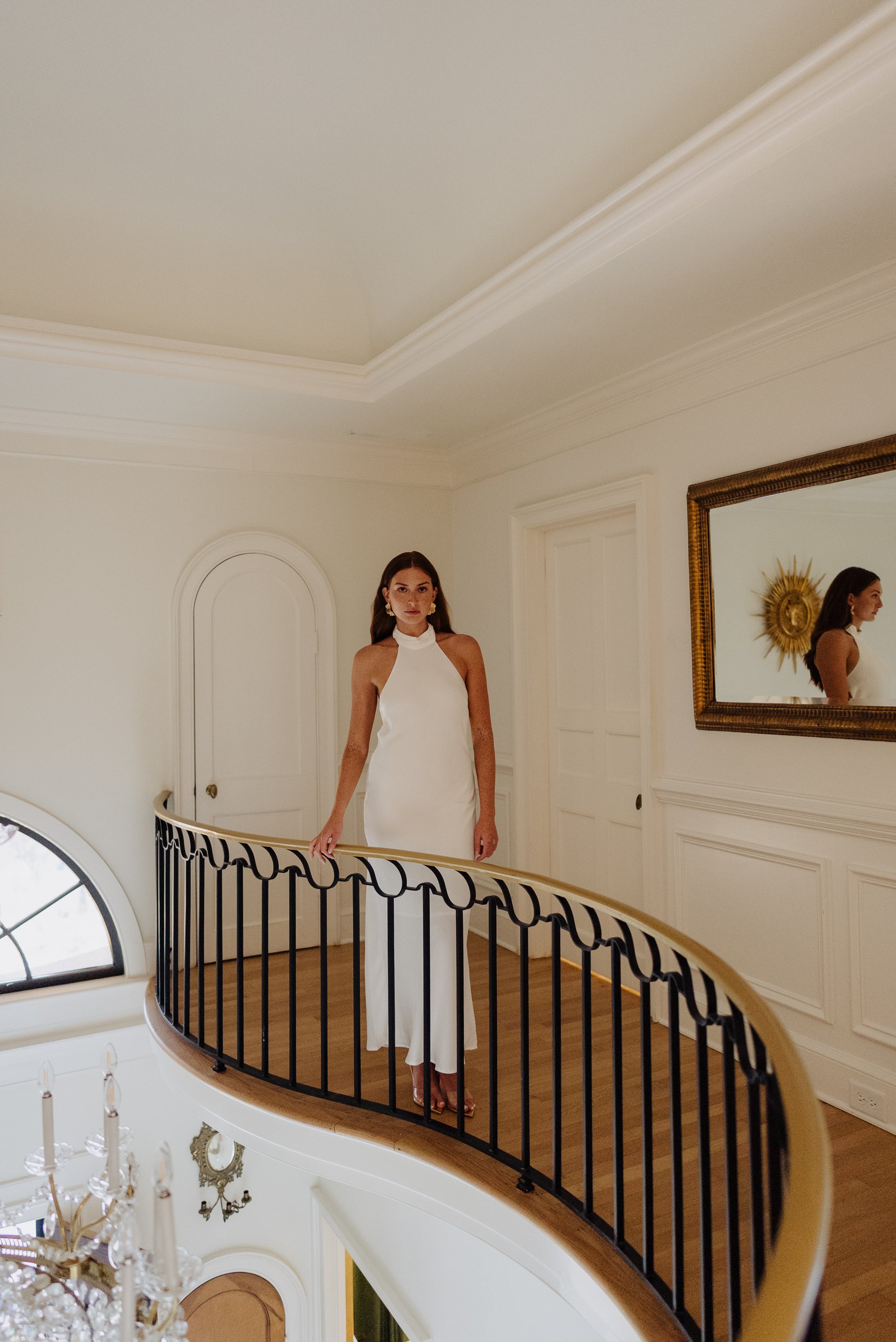 Woman in a white dress standing on a staircase in an elegant interior setting.