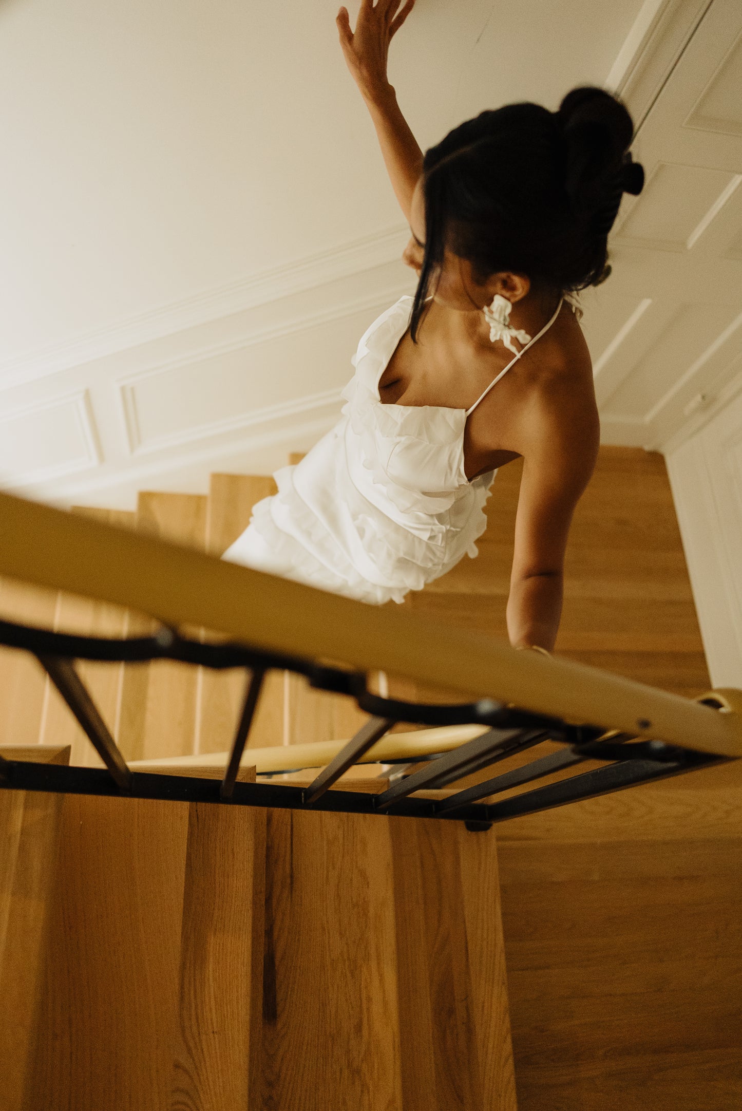 Woman in a white dress standing on a wooden staircase with a white wall in the background