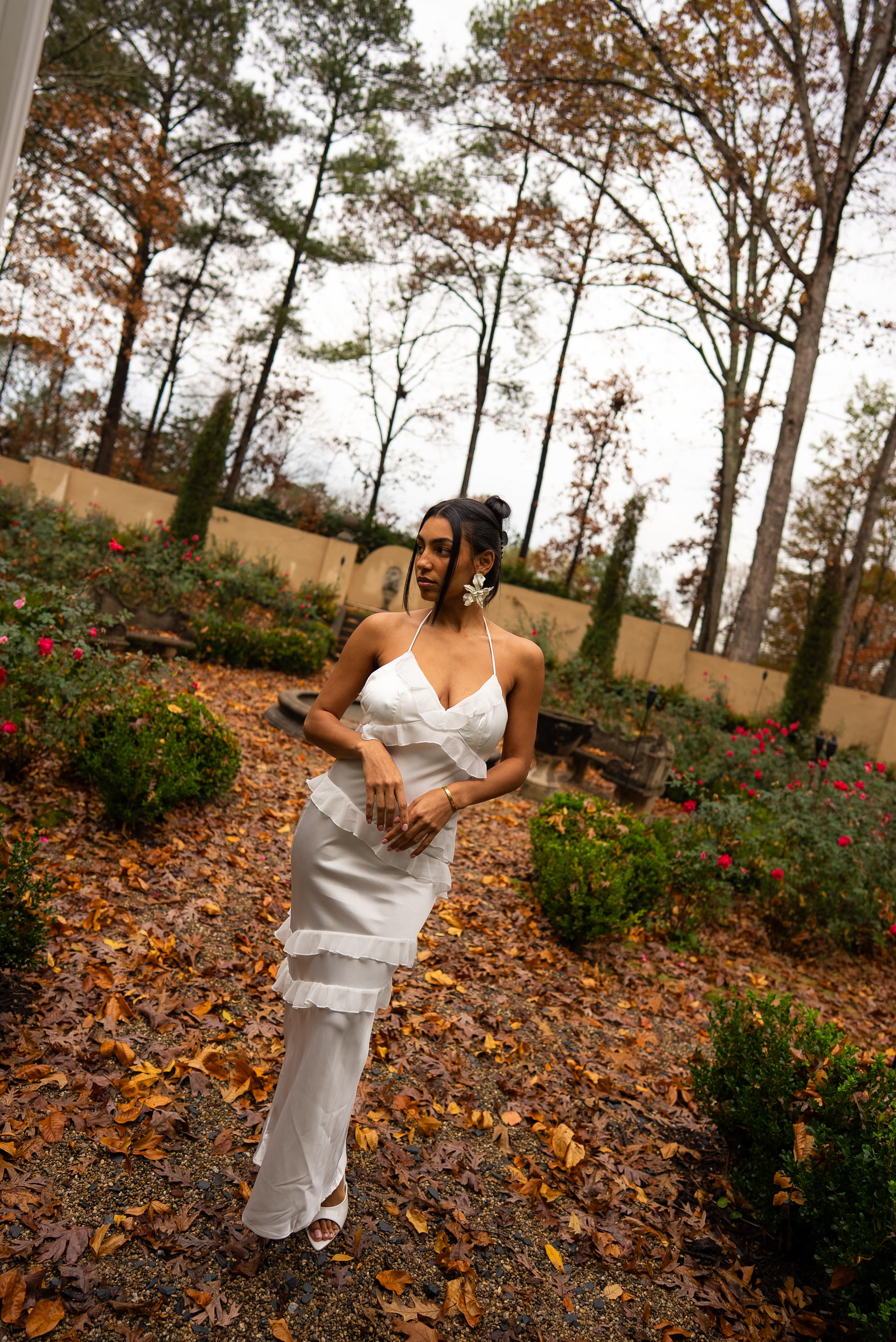 Woman in a white dress standing in a garden with trees and flowers in the background