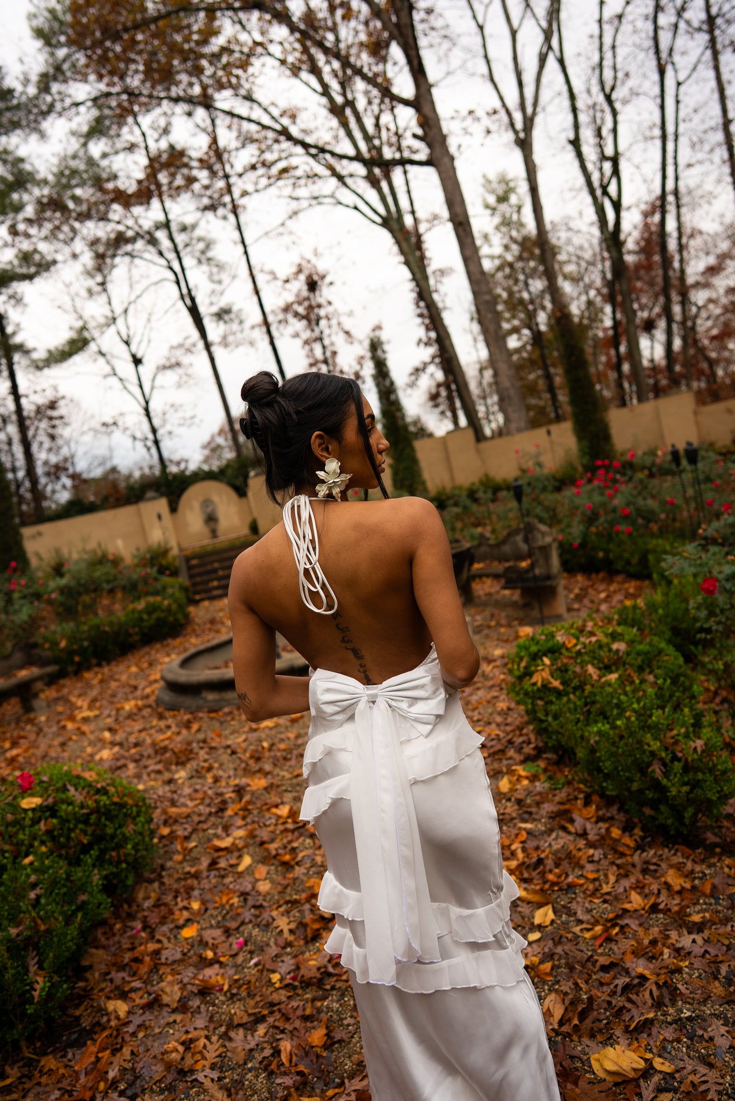 Woman in a white dress standing in a garden with trees and a fountain in the background